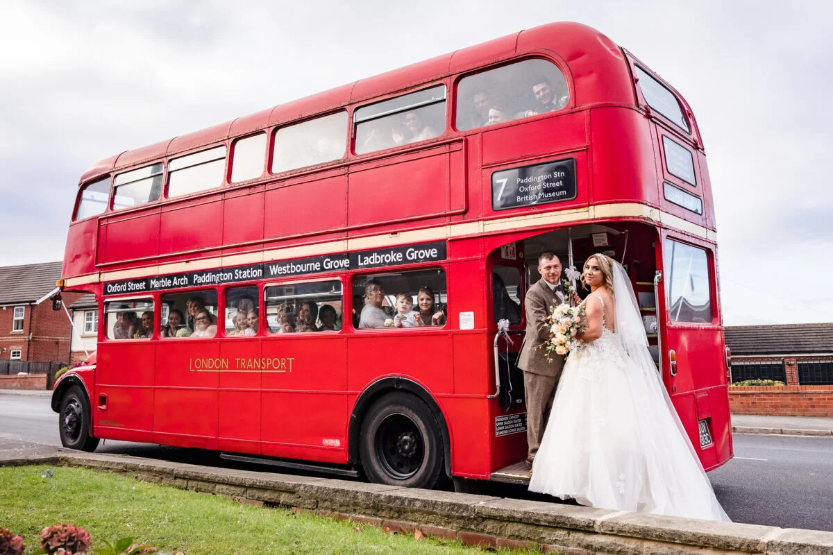 A bride and groom standing next to a red double decker bus.