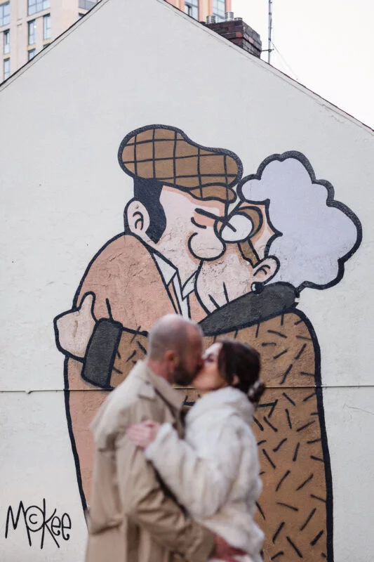A man and woman kissing in front of a mural.