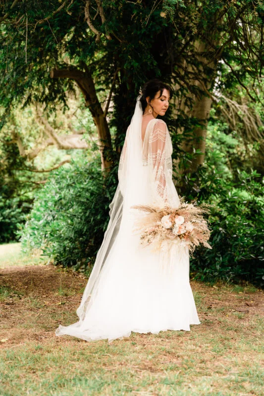 A bride in a wedding dress standing in a wooded area.