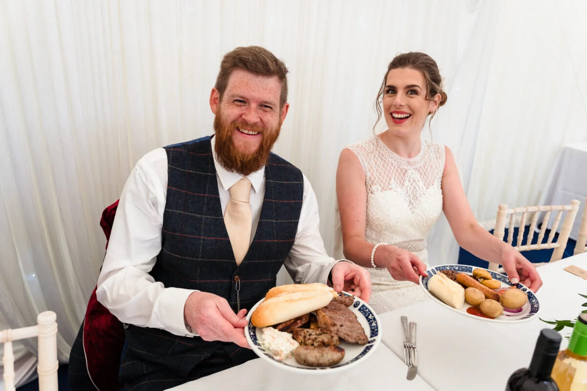 A bride and groom holding plates of food.