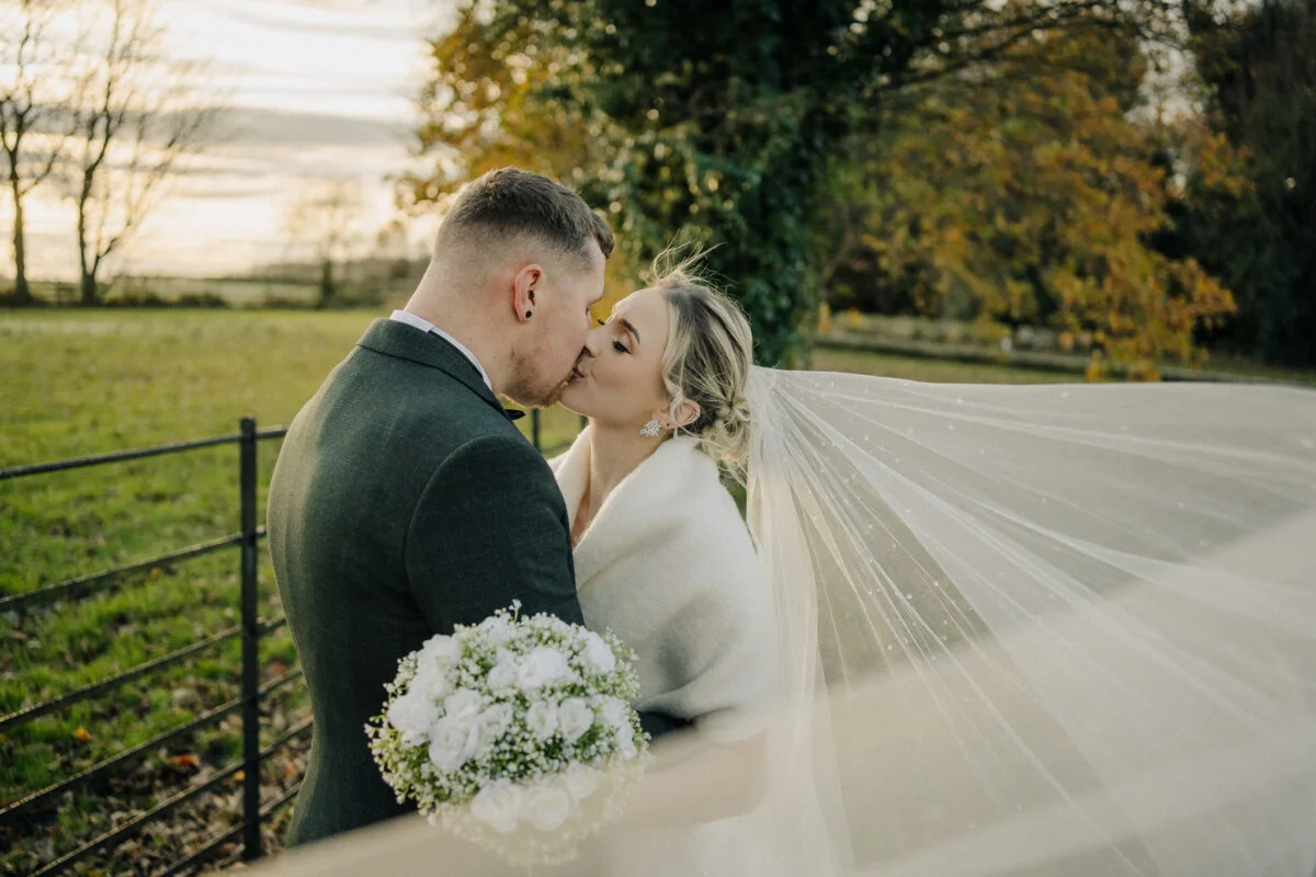 A bride and groom kissing in front of a fence.