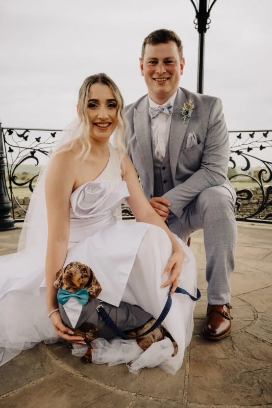 A bride and groom posing with a dachshund.
