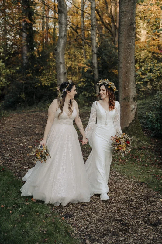 Two brides walking down a path in the woods.