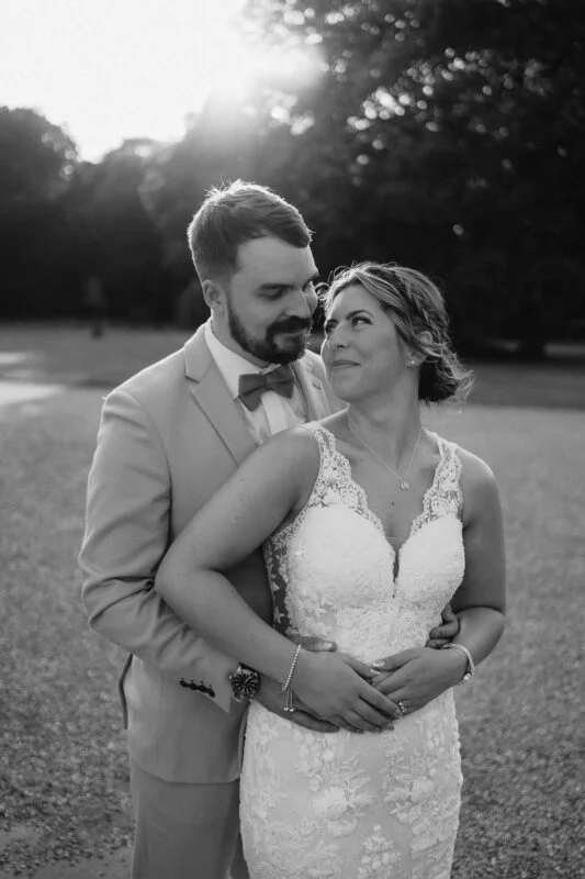 A bride and groom embracing in front of a tree.