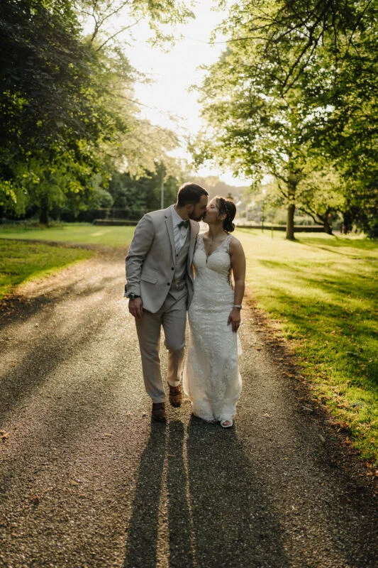 A bride and groom are walking down a path in the woods.