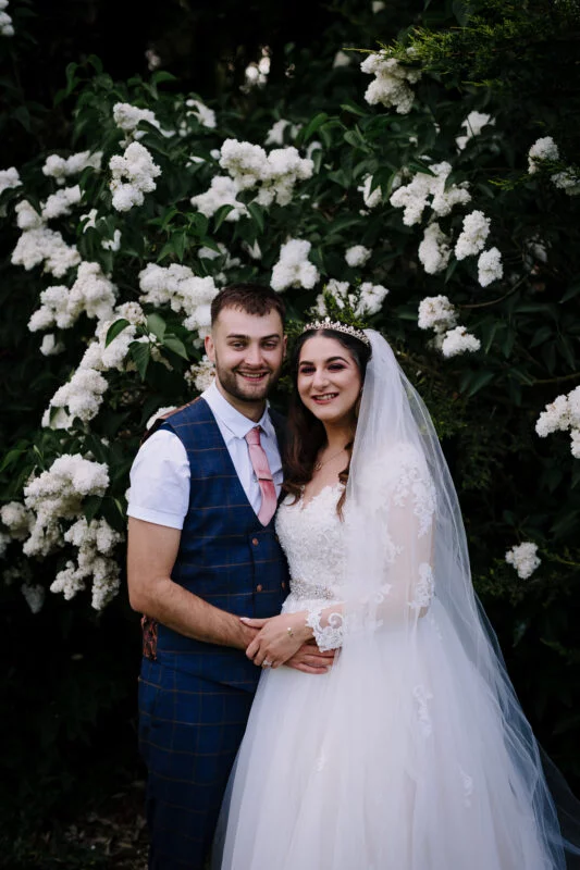A bride and groom posing in front of white flowers.