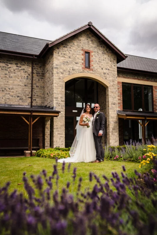 A bride and groom standing in front of a stone building.