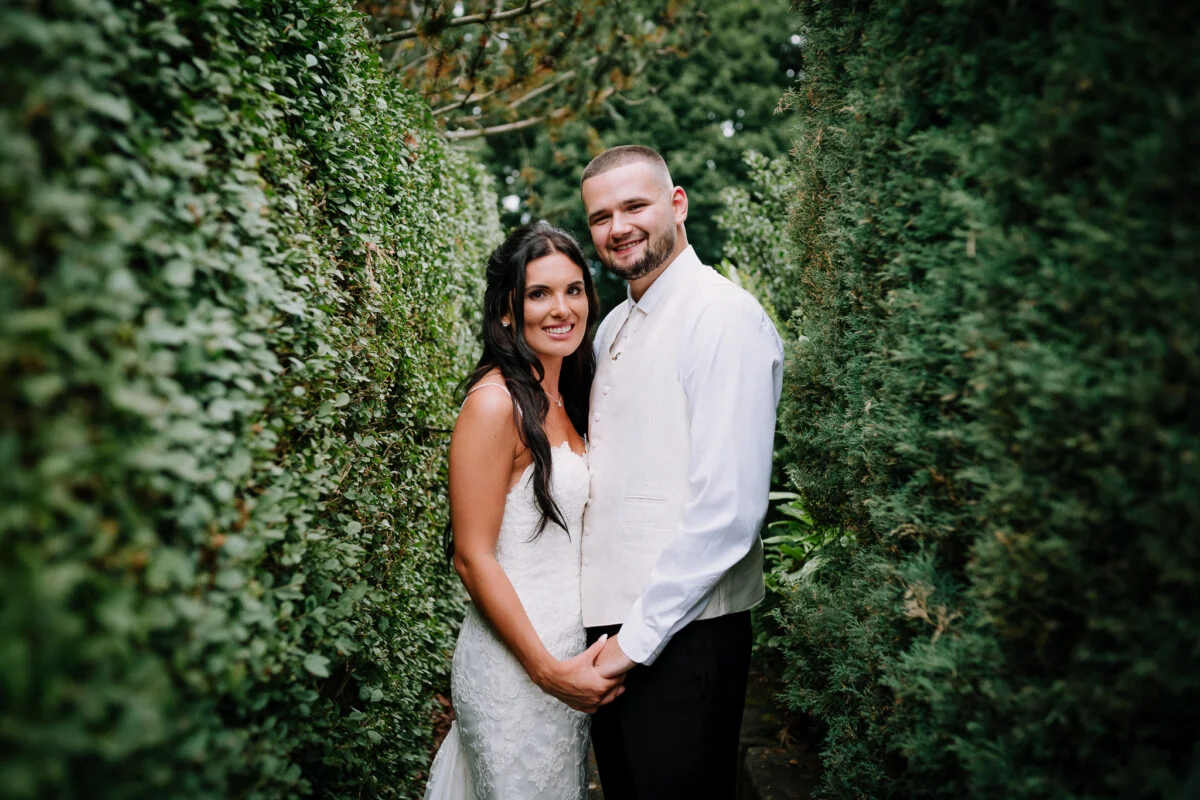 A bride and groom posing for a photo in a hedge.