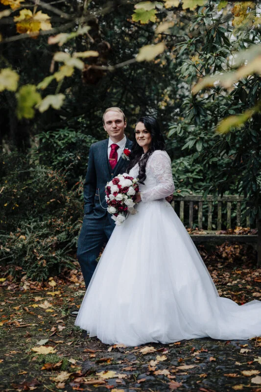 A bride and groom posing for a photo in the autumn leaves.