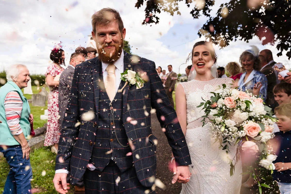 A bride and groom walk through confetti at their wedding.