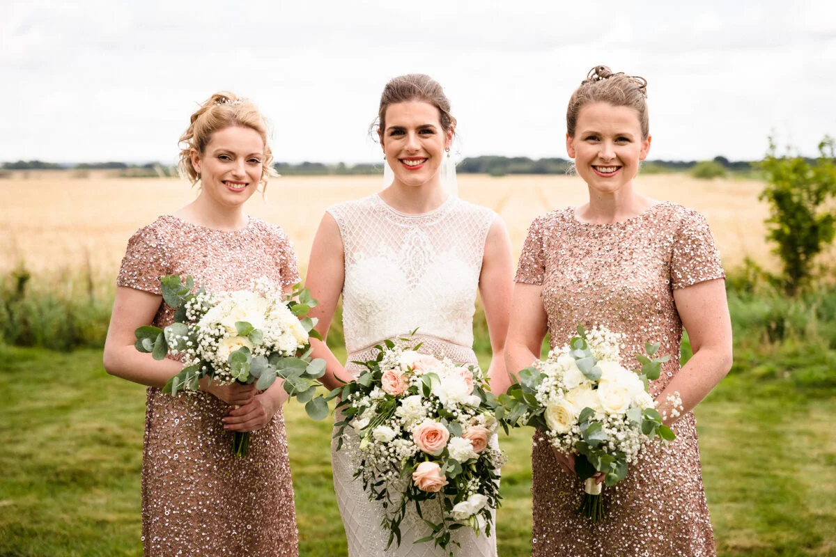 Three bridesmaids holding bouquets in a field.