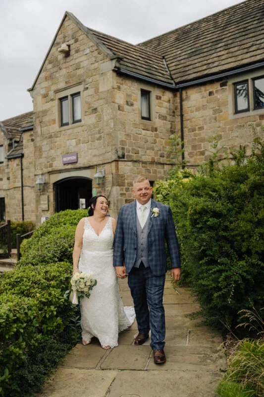 A bride and groom walking in front of a stone building.