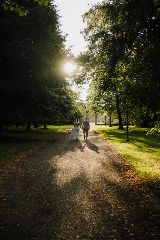 A bride and groom walking down a path in a park.
