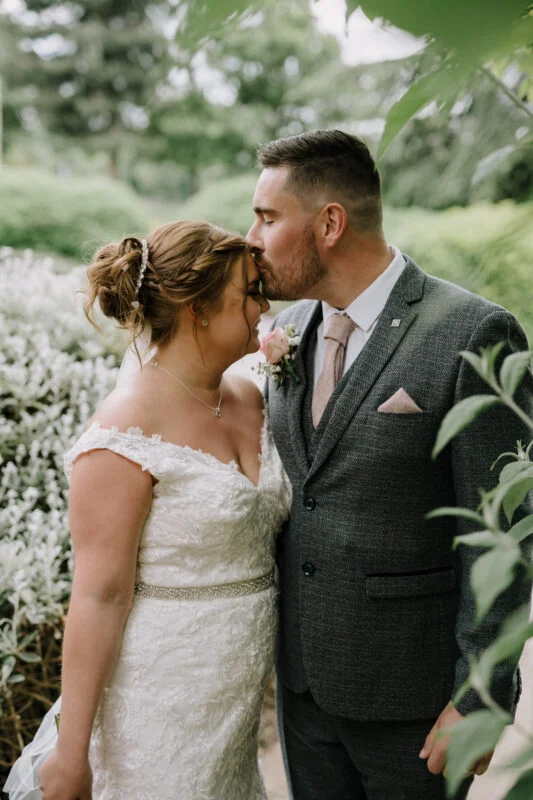 A bride and groom kissing in a garden.