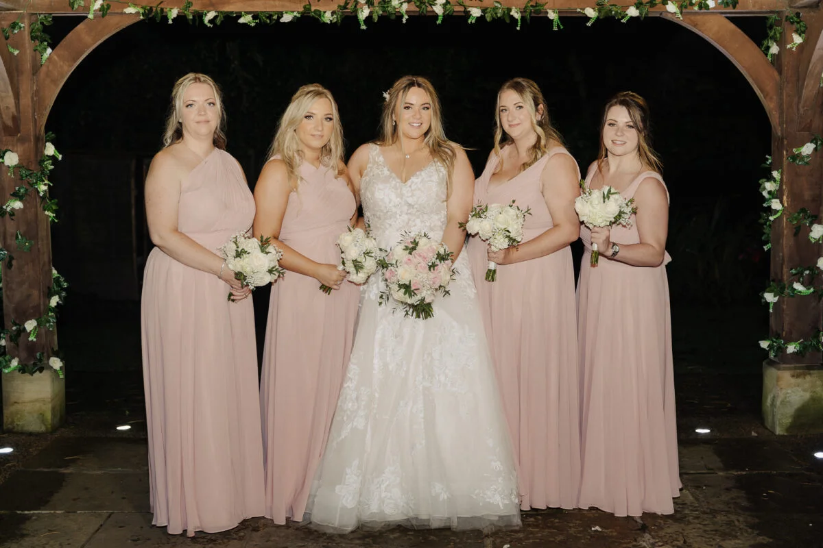 A group of bridesmaids standing in front of a pergola.