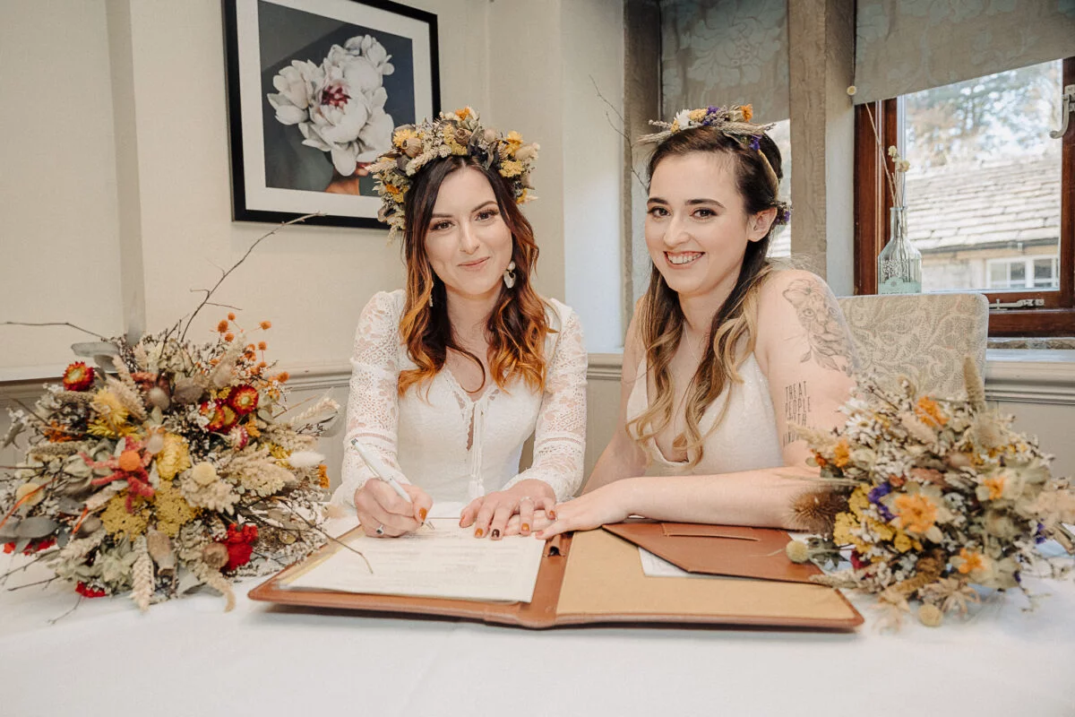 Two brides signing their wedding vows at a table.
