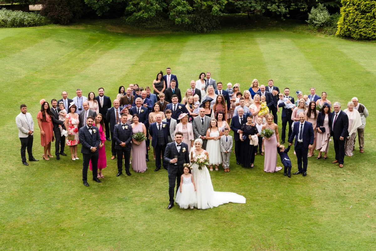 A wedding party posing in a circle on a grassy field.