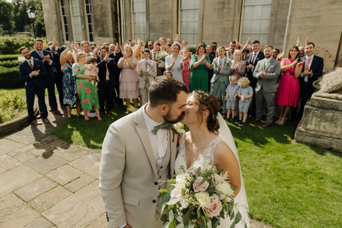 A bride and groom kissing in front of their wedding guests.