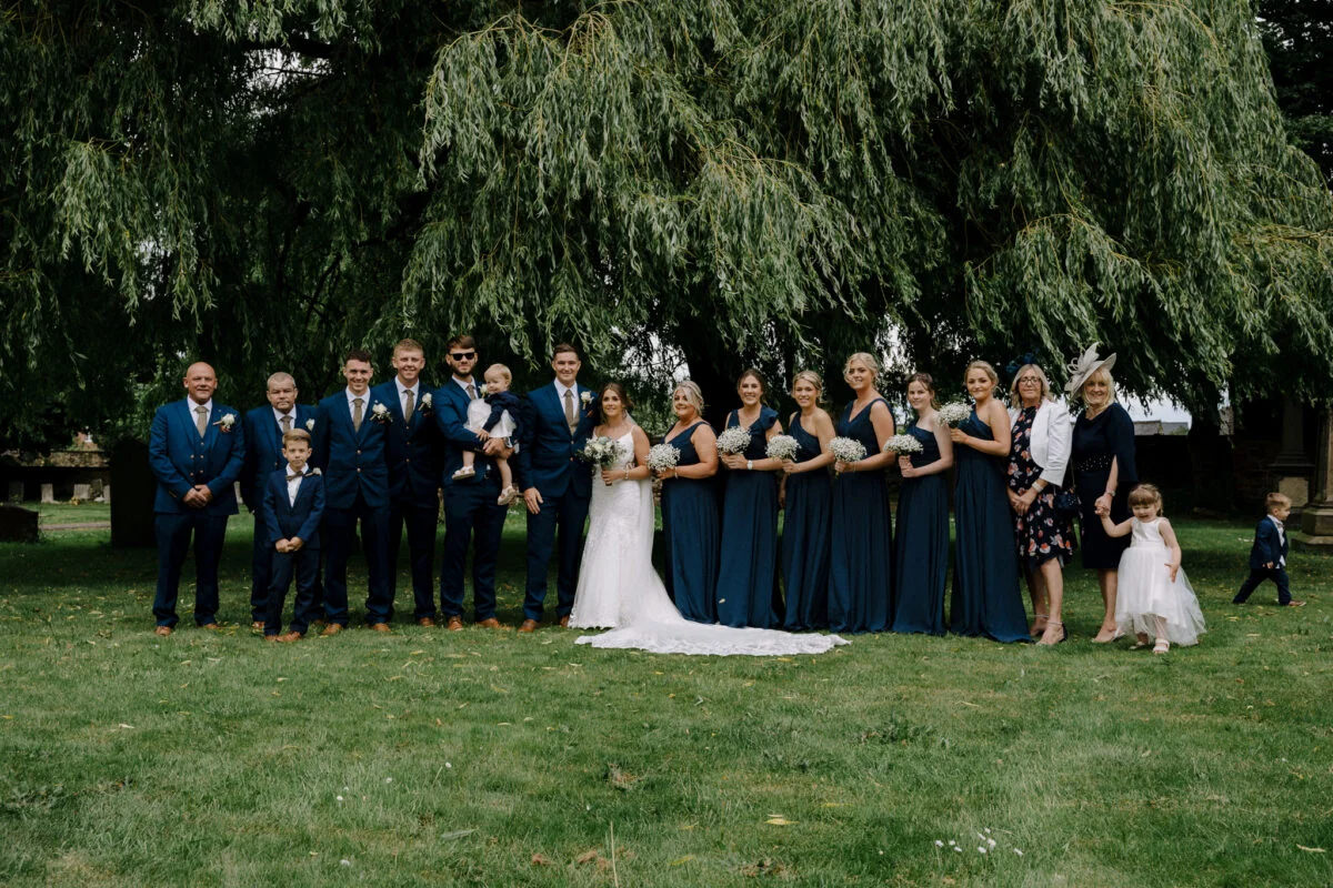 A wedding party posing in front of a willow tree.