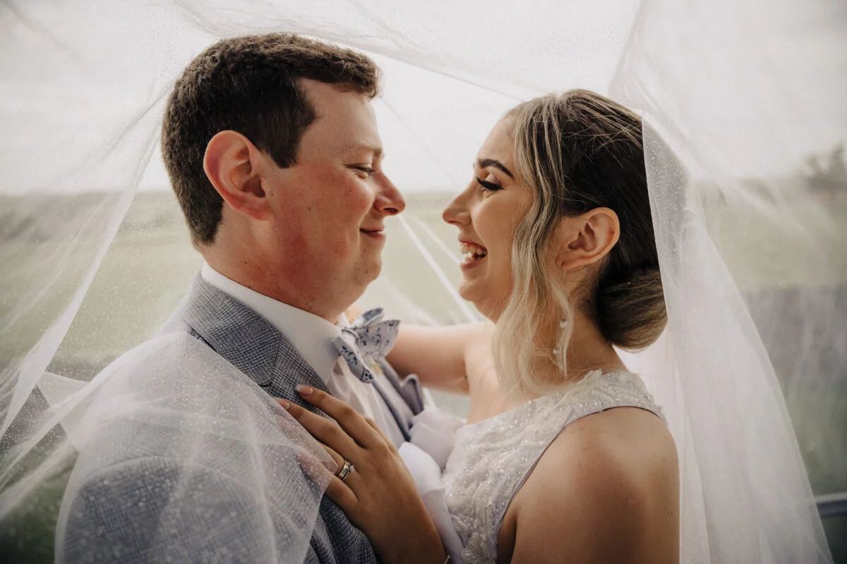 A bride and groom smiling under a veil.