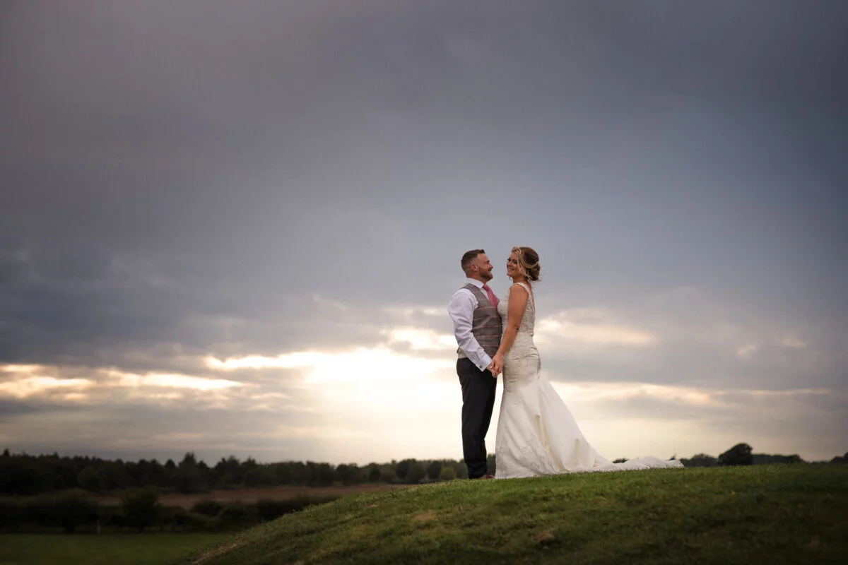 A bride and groom standing in front of a cloudy sky.