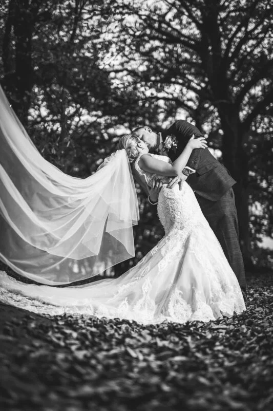 Black and white photo of a bride and groom kissing in the woods.