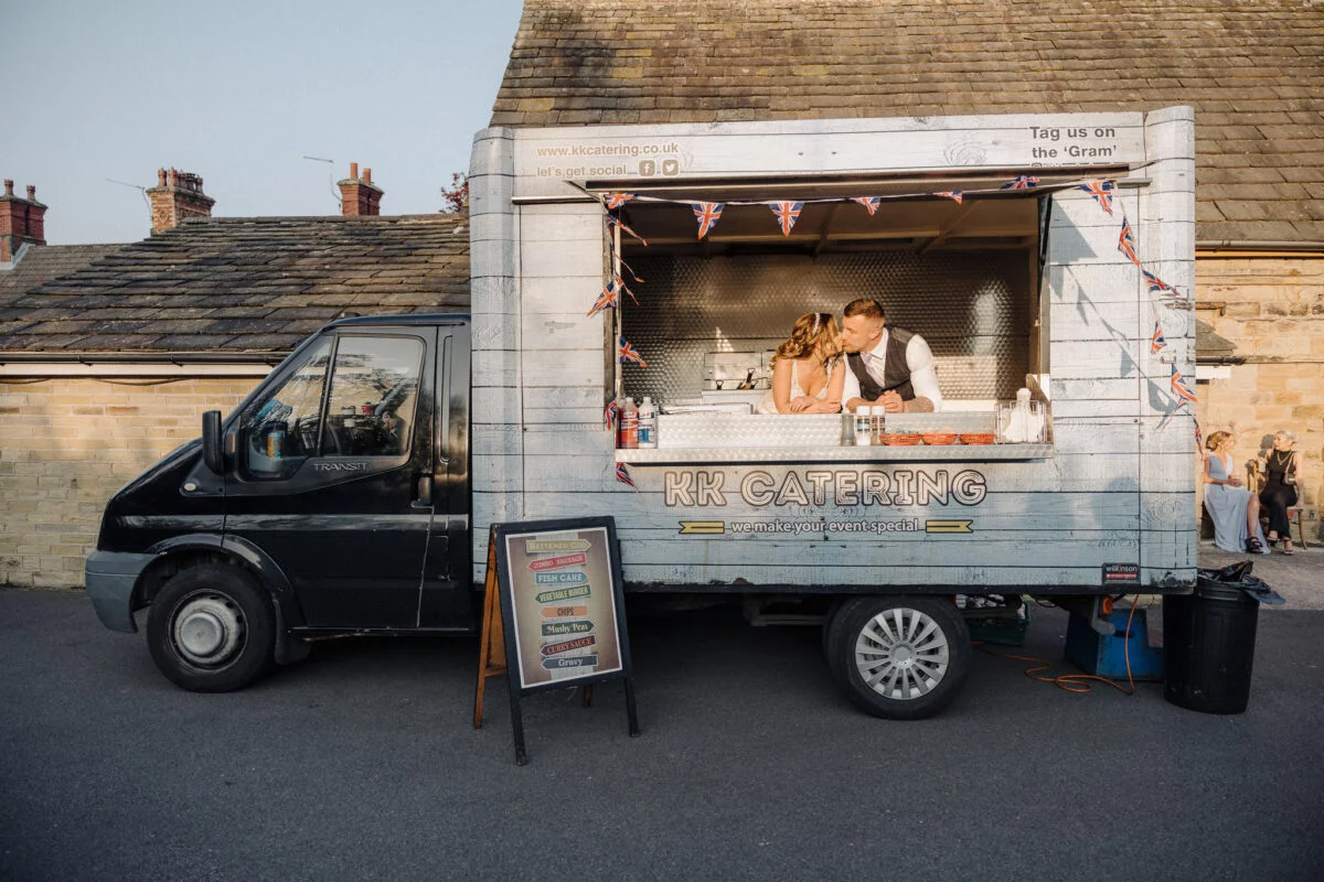 A bride and groom standing in front of a food truck.