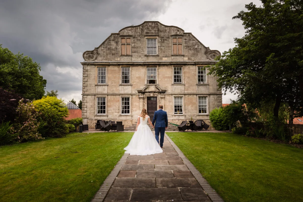 A bride and groom walking down a path in front of a large building.