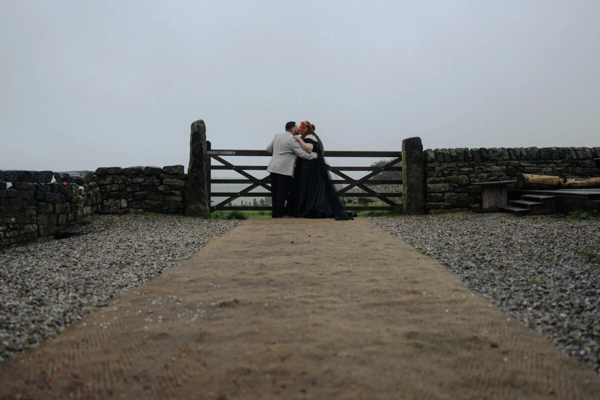 A bride and groom kissing in front of a stone gate.