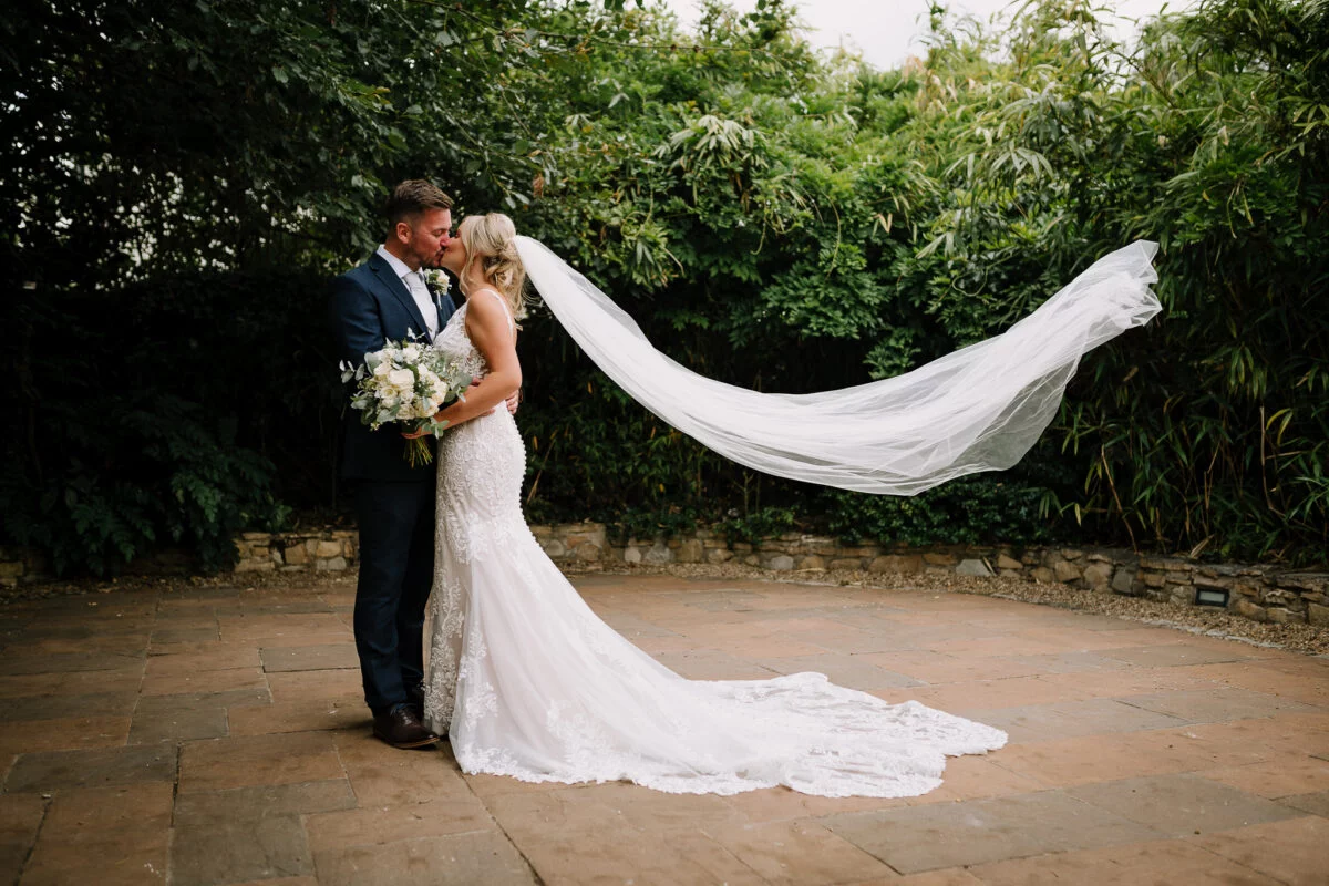 A bride and groom kissing in a courtyard with a veil blowing in the wind.