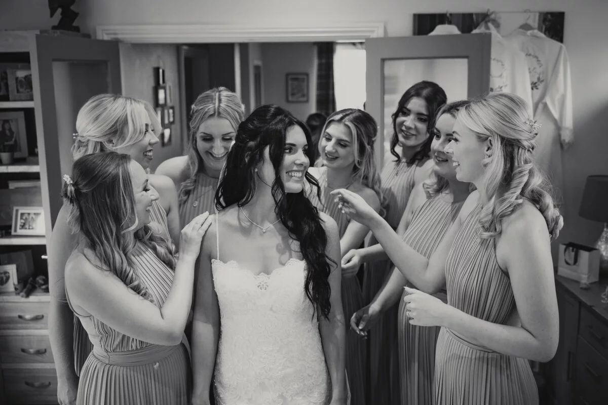 A bride and her bridesmaids look at each other in a mirror.
