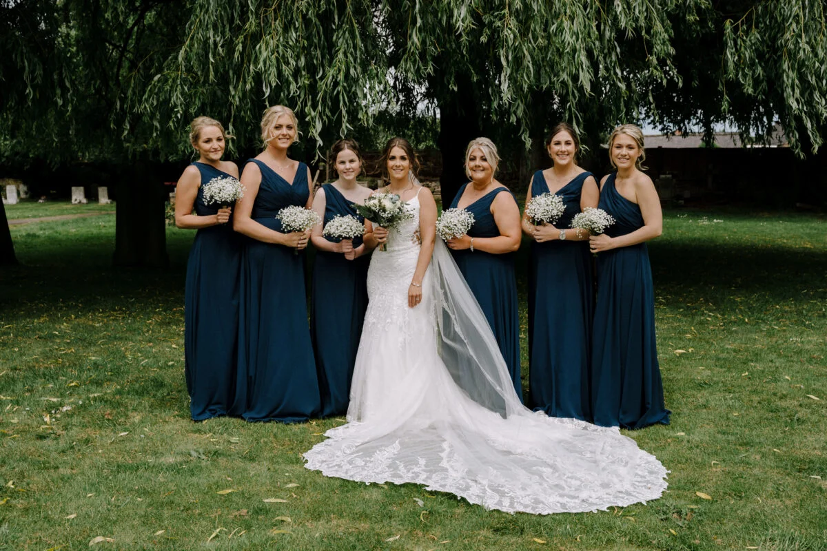 The bride and bridesmaids pose in front of a willow tree.