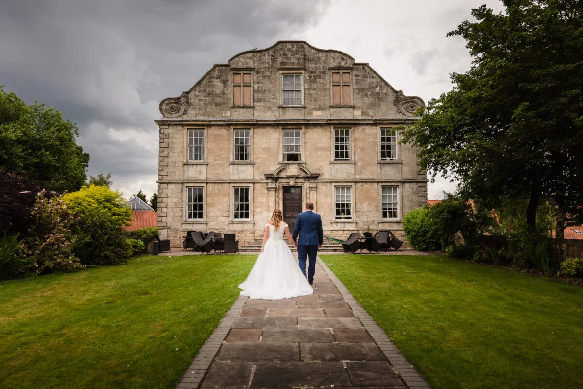 A bride and groom walking down a path in front of a large building.