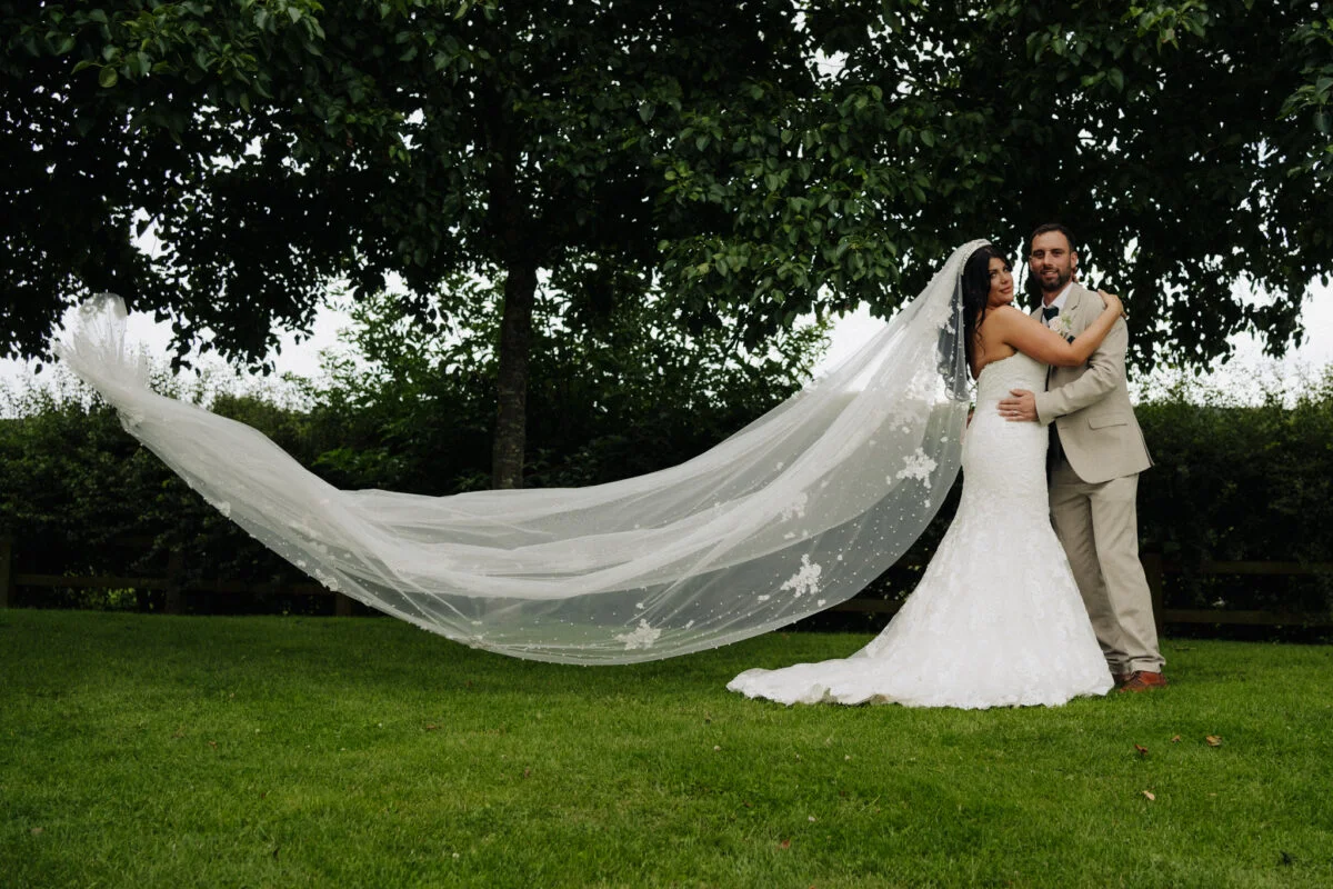 A bride and groom with their veil blowing in the wind.