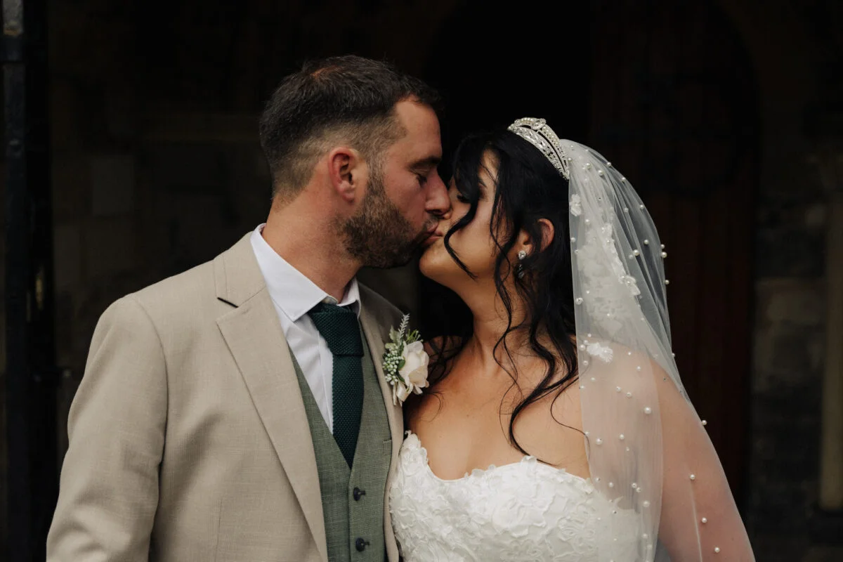 A bride and groom kissing in front of a church.