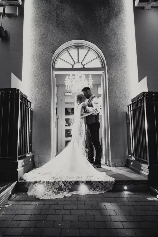 A bride and groom kissing in front of a building at night.