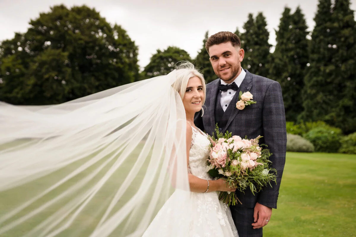 A bride and groom with their veil blowing in the wind.