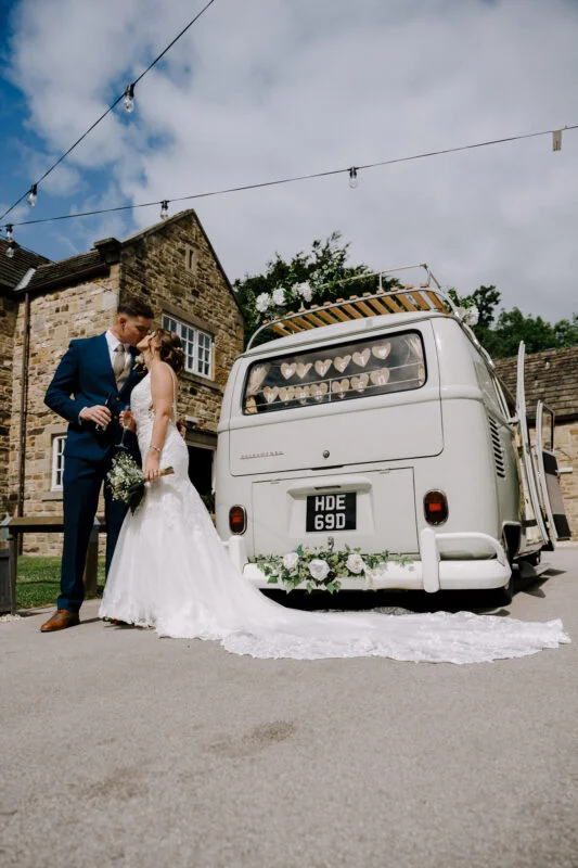 A bride and groom pose next to a vintage vw bus.