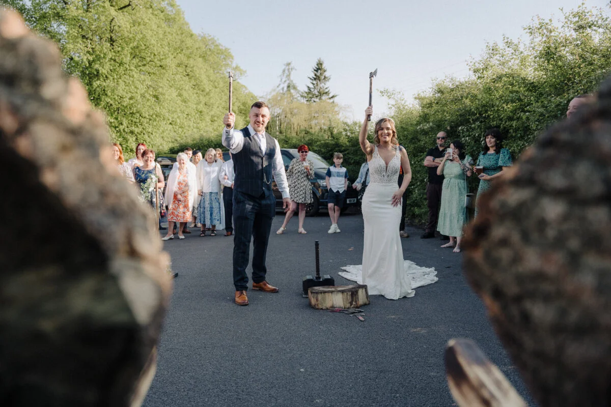 A bride and groom are holding sticks in front of a tree.
