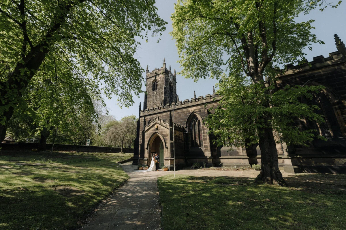 A bride walks down a path in front of a church.