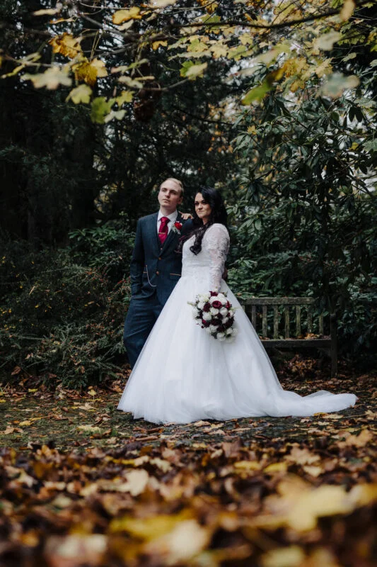 A bride and groom posing for a photo in the autumn leaves.
