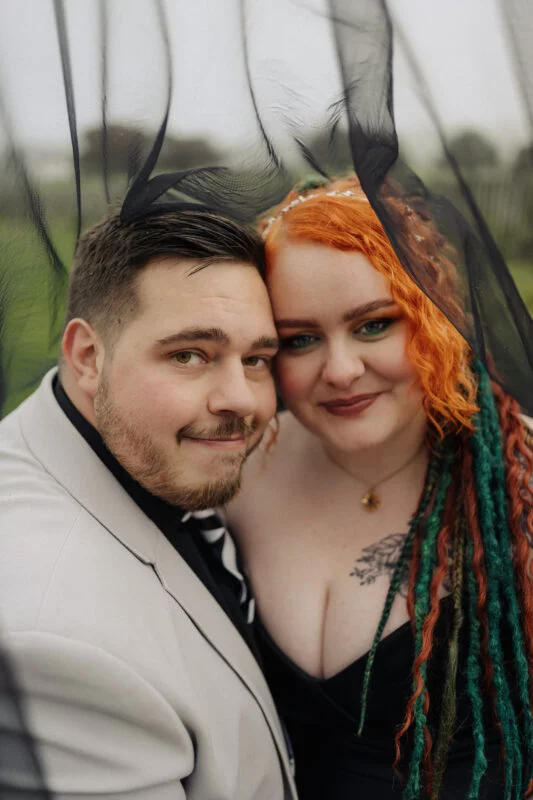 A man and woman posing for a photo under a veil.