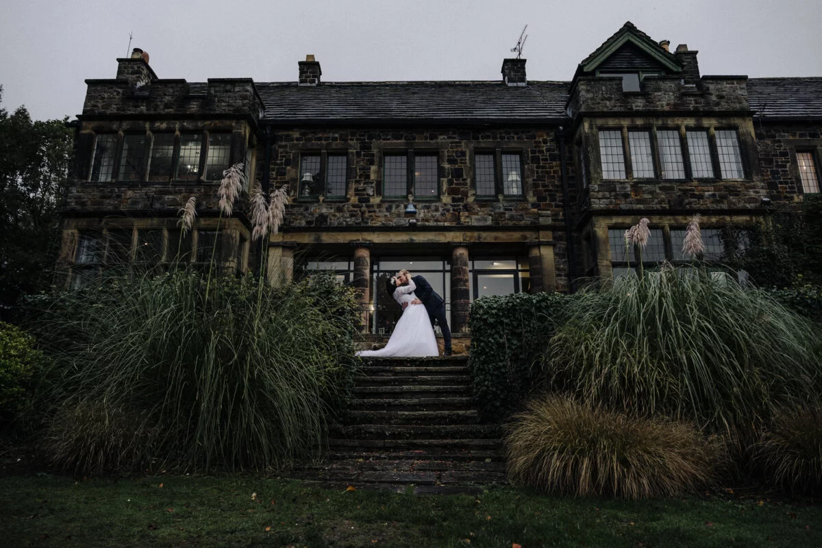 A bride and groom standing in front of a large mansion.