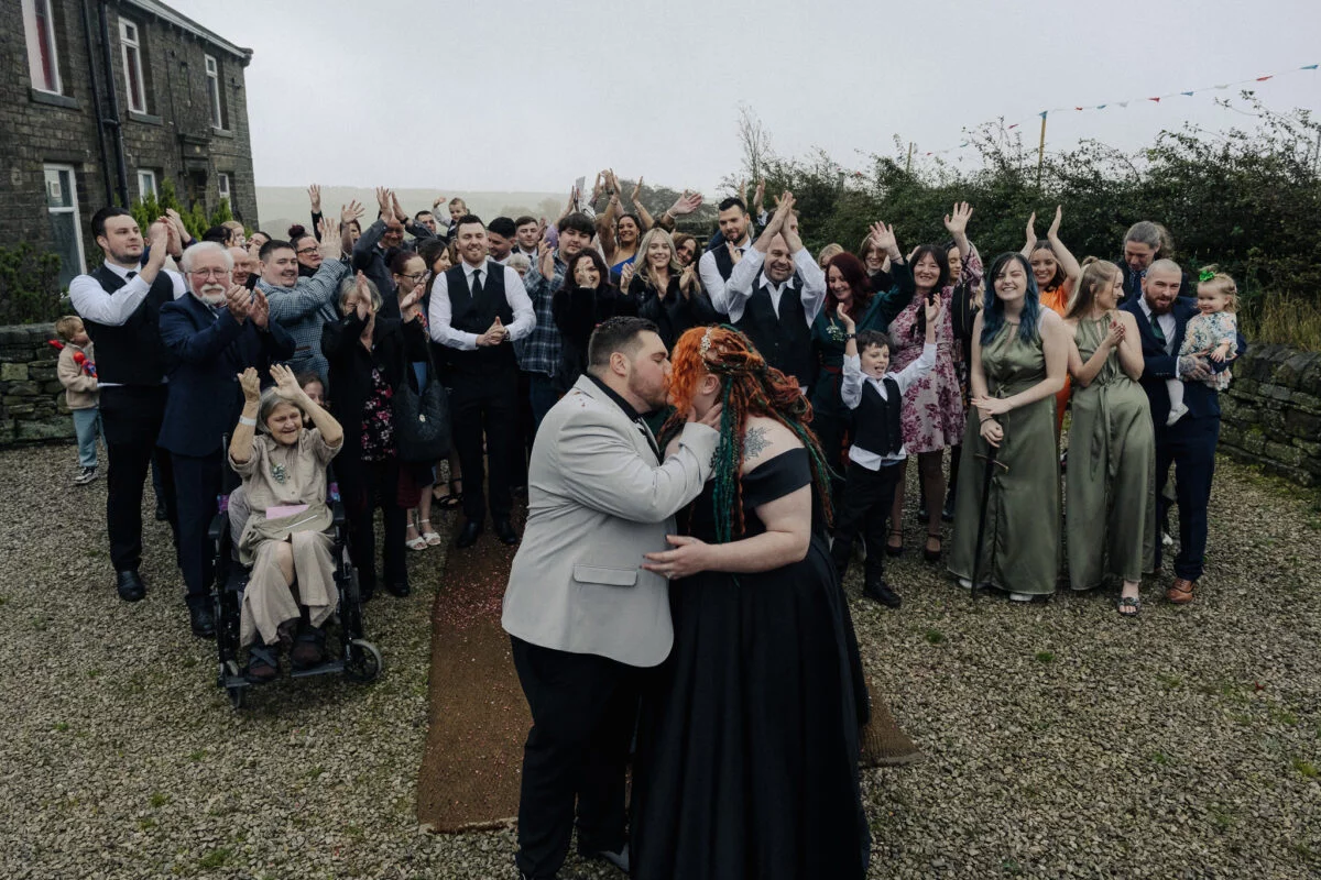 A bride and groom kiss in front of a large group of people.