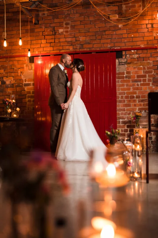 A bride and groom kissing in front of a red brick wall.
