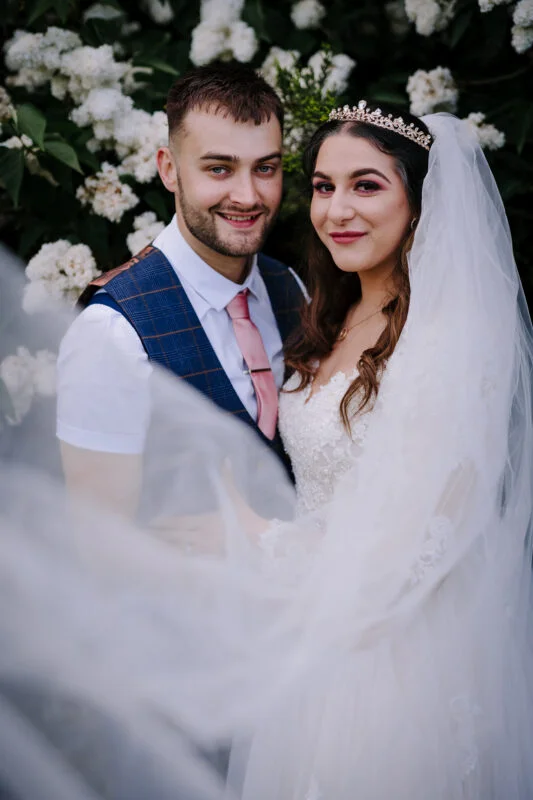 A bride and groom posing in front of white flowers.