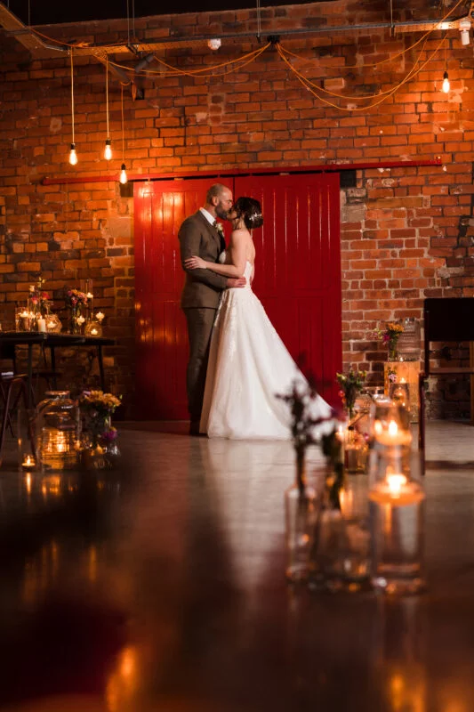 A bride and groom standing in front of a brick wall with candles.
