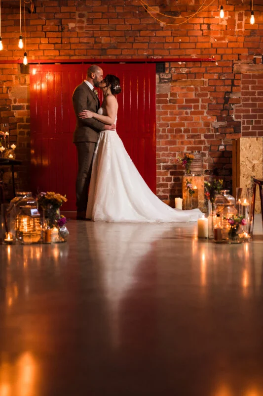 A bride and groom standing in front of a brick wall with candles.