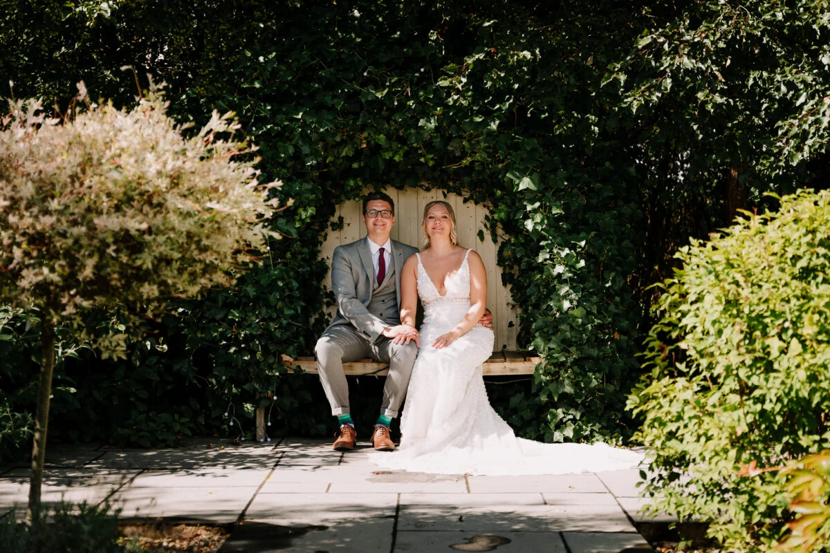 A bride and groom sitting on a bench in a garden.