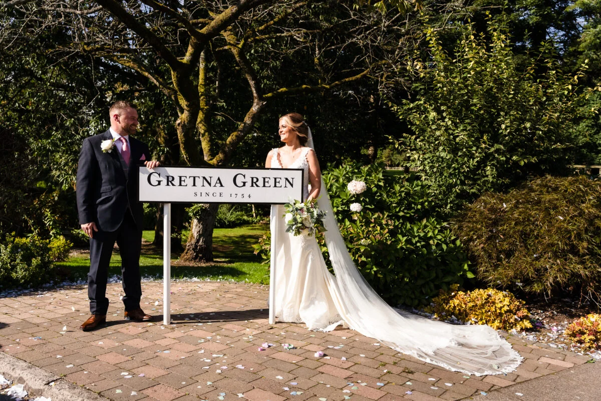 A bride and groom standing next to a sign for greta green.
